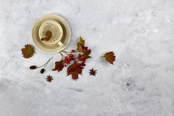 Autumn composition. Cup of coffee with cinnamon, autumn leaves and rowan berries on grey background. Flat lay, top view.  