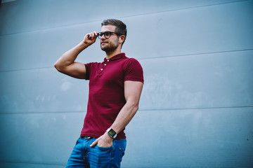 Stylish handsome man dressed in trendy casual outfit fixing eyeglasses while looking away.Young man 20 years old in optical spectacles standing against promotional background for advertising