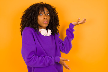 Beautiful European girl pointing aside with both hands showing something strange and saying: I don't know what is this. Standing against gray background. Advertisement concept.