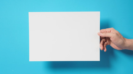 Obraz premium Hand is holding the A4 paper on blue background.