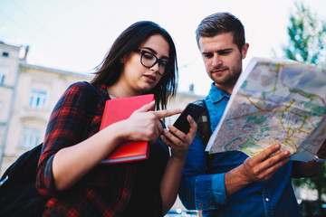 Two students travelling in new town with map and modern telephone to find right destination.Young tourists searching direction in online website using smartphone and free 4G internet connection