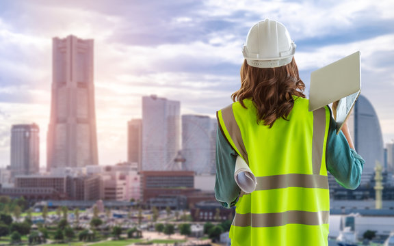 Female Civil engineer with computer and blueprint is standing infront of Japan Yokohama Skyscraper City for city development.