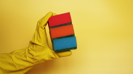 Hand in glove holding few washing sponges on yellow background - amount of housework concept