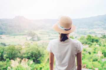 Fototapeta premium Asian attractive young woman traveler tourist hiking wearing hat back view standing silhouette looking at mountain nature landscape view scenery, hot summer wearing hat feeling peaceful joyful happy