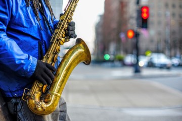 A closeup of a street saxophonist playing downtown with the street blurred in the background.