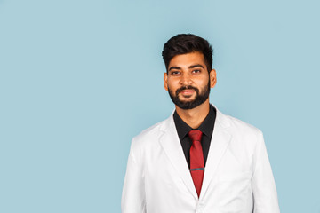 Handsome modern indian / asian doctor with stethoscope, tie and white coat on blue background