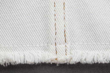 white denim fabric, connecting parts with various seams with brown threads, raw edge with fringe