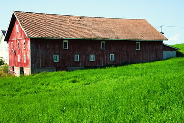 Obraz premium Old and worn red barn with lush green pasture in the foreground.