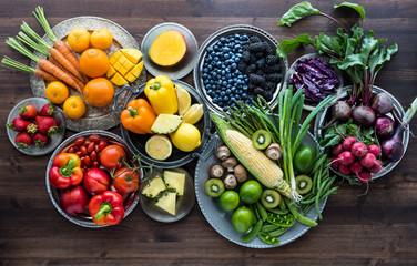 Rainbow fruit and vegetable flat lay arrangement against a dark wooden background.