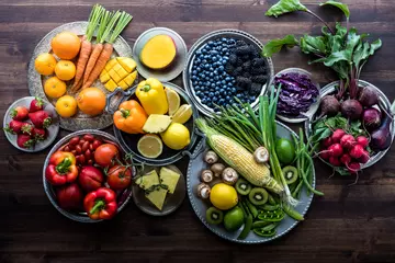  Various fresh organic fruits and vegetables on metal plates in rainbow colours against a dark wooden background. © Carey