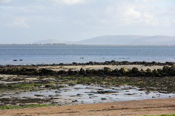 Sea through rocks and sand and mountains in the background in Galway