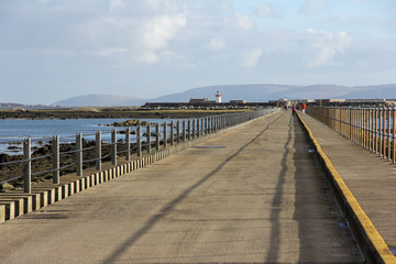 Asphalt road to the lighthouse with railings and the sea next to Galway