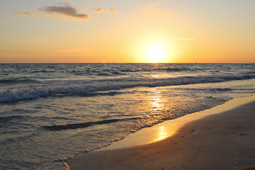 Fototapeta na wymiar Sunset illuminates tranquil waves and shoreline along the beach in Lido Key off Sarasota, Florida. Glowing yellow sun sets over calm Gulf of Mexico waters near Siesta Key. Summer nights in FL.