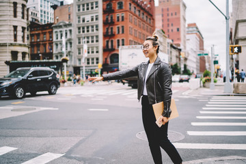 Attractive prosperous asian female blogger dressed in casual clothes trying to catch taxi while walking at spring street.Emotional hipster girl gesturing for stopping public transport outdoors