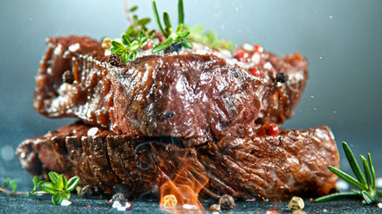 Close-up of tasty beef steak on black stone table, fire flames in foreground