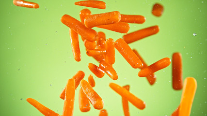 Flying baby carrots isolated on light green background, close-up.