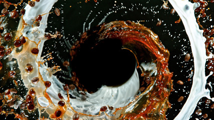 Fresh roasted coffee beans with milk splash flying in the air in vortex shape, isolated on black...