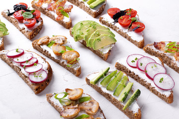 Bruschetta assortment with cream cheese, vegetables, mushrooms and bacon on the white table....
