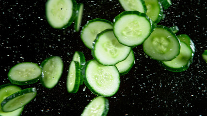 Freeze motion of flying cucumber in the air with water splashes, isolated on black background