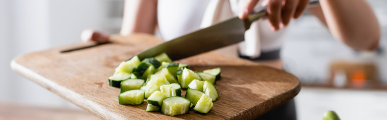 panoramic crop of woman holding cutting board with sliced cucumber and knife