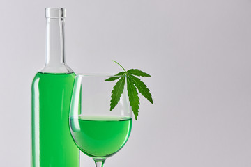 A glass and a bottle of green weed wine on gray background with copy space