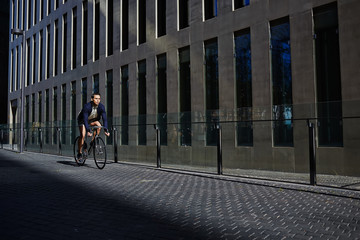 Stylish hipster man riding on fixed gear bike, young handsome man ride on bicycle in modern city zone, attractive young man ride on fixed gear bicycle looking away