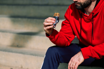 Close-up of runner sitting on the stairs and eating energy bar after running.