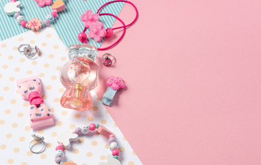 Children's flat lay. Perfume in the form of candy, children's jewelry and hair accessories on a pink background. Accessories for little girls