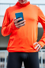 Runner using smart phone outdoors. He is holding hand on the hip.