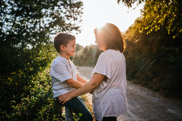 Fototapeta premium Mother kisses 6-year-old son on forehead in field at sunset