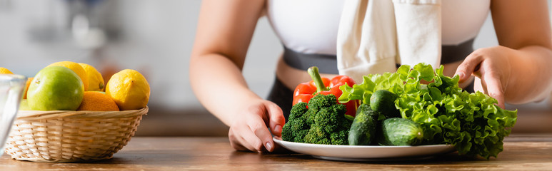 panoramic crop of woman touching plate with vegetables near lemons