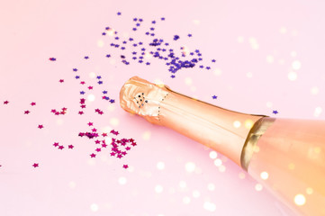 Champagne bottle with confetti on pink background. Blurred effect. Creative space for Christmas design. 