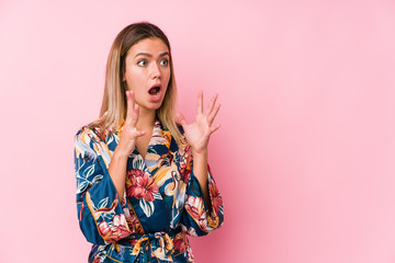 Young caucasian woman wearing pajamas shouts loud, keeps eyes opened and hands tense.