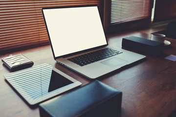 Laptop computer with white blank copy space screen for text message or publicity content lying on wooden table with digital tablet and stylish accessories,electronic business and distance work concept