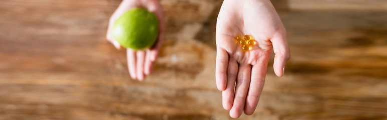 panoramic crop of woman holding apple and food additives in capsules