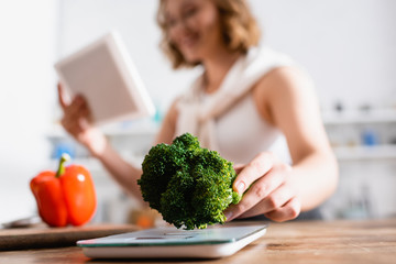 selective focus of woman holding broccoli near kitchen scales