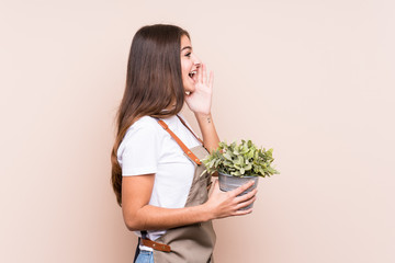 Young gardener caucasian woman holding a plant isolatedshouting and holding palm near opened mouth.