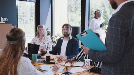 Group of happy young diverse start-up business people brainstorming at modern office, all wearing COVID-19 face shields.