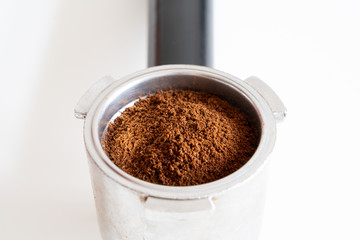 Portafilter filled with ground coffee on white background