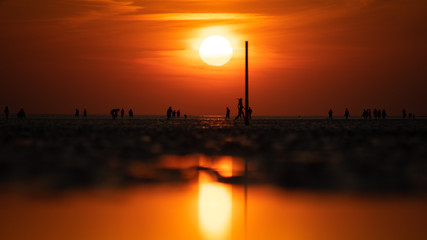 People on the beach in the sunset and it's reflection in the Wadden Sea.