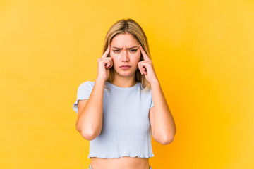 Young blonde caucasian woman isolated on yellow background focused on a task, keeping forefingers pointing head.