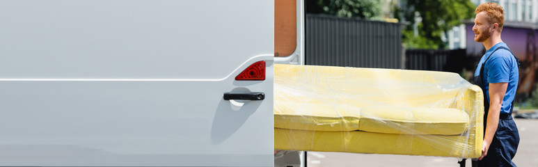 Horizontal image of loader holding couch near truck with open doors on urban street