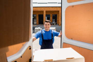 Selective focus of loader standing near cardboard box and doors of truck on urban street