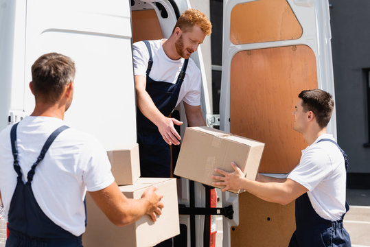 Selective focus of loader giving cardboard box to colleague while unloading packages from truck on urban street