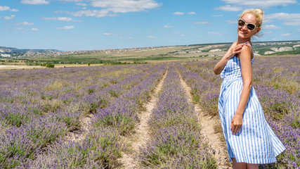 A beautiful woman on a lilac field, a young with a kind look, sunglasses, standing joyful with a good appearance, stands