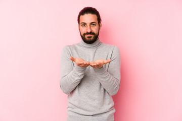 Obraz premium Young long hair man isolated on a pink background holding something with palms, offering to camera.