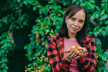 Pretty young woman holds apricots in her hands. Adult female with ripe fruits smiling and looking at camera on background of apricot tree.