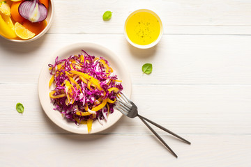Light summer salad of red cabbage, onions and yellow bell peppers, salad in a plate on a white wooden background, olive oil with spices for dressing, top view