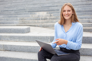 Education, freelance and people concept. Portrait of smiling young European student woman with happy face, sitting on stairs and pointing at the screen laptop, looking at camera. Empty copy space.