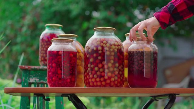 Jars with kompot on table. Sealed glass jars with kompot placed on table near flowers and fruits on summer day in garden